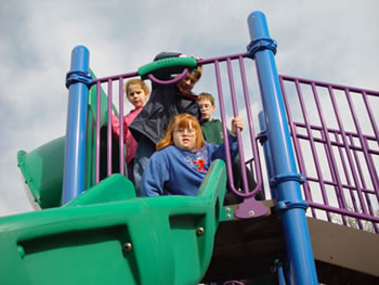 A girl sits to enter a slide on an elevated platform while surrounded by three friends.
