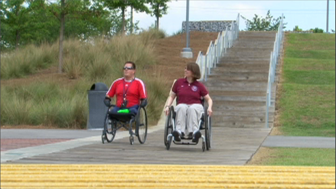 two wheelchair users pushing at a park