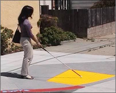a woman with a walking cane for visual impairment feels truncated domes on a curb cut ramp