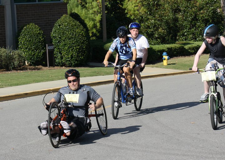 a group of individuals ride together on a bicycle, handcycle, and tandem bicycle