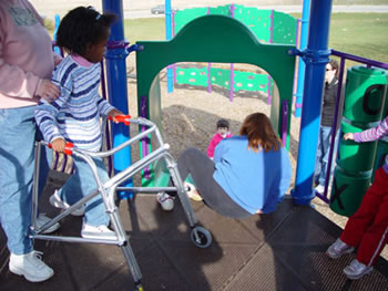 A child using a walker waits on the elevated platform for her turn to go down the slide.