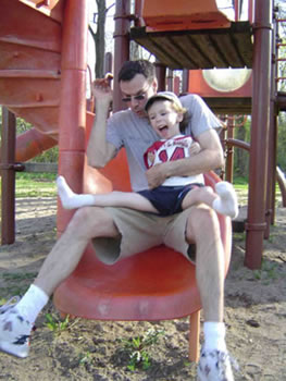 A father descends a spiral slide with his son on his lap.