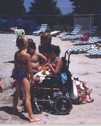 A girl in her wheelchair surrounded by family at the pool.