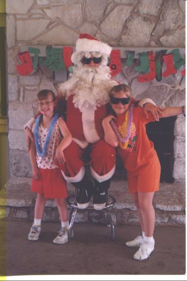 Two girls posing with Santa Clause in front of a fireplace.