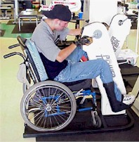 Photo of a young man who uses a wheelchair working the upper and lower extremities on a power trainer