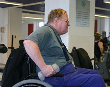 A man seated a wheelchair is demonstrating the start position for a Double Arm Triceps Kickback with Free Weights exercise
