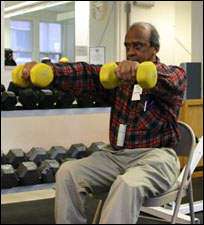 A man is seated demonstrating the end position for a Front Raise with Free Weights - Shoulders exercise.