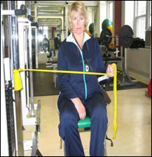 A woman is seated demonstrating a start position for a External Rotation with Thera-Band® exercise