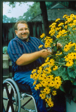 Man using wheelchair pruning plants growing in planter at chest height