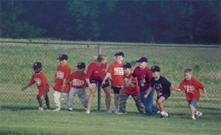 A group of young boys in their baseball shirts and caps on a field with an adult.