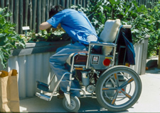 Young man using power wheelchair tending a 24-inch high wood frame raised bed.