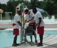 Three lifeguards stand near an outdoor pool inspecting the  pool lift.