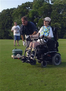 3 people on a golf course: two men and one teenager who uses a power wheelchair.
