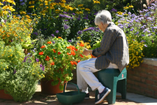 Woman tending flowers in 24 inch high round planter while sitting on a small lightweight portable seat 18