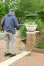 Older man watering plants using a long stick-like hose attachment