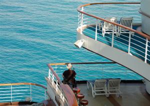 A man using a wheelchair is looking out into the ocean while on a ship.