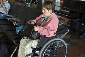 A woman that uses a wheelchair is looking inside her bag while in the airport.