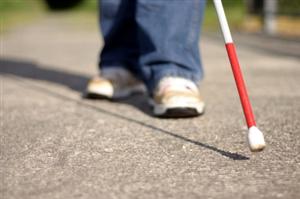 A person with a visual impairment is walking with a walking cane.