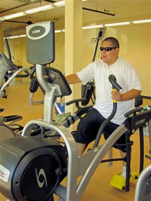 A man with a visual impairment is using an elliptical trainer.
