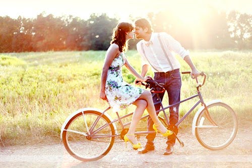 A male and female couple are kissing on a tandem bicycle