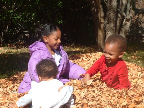 Three children play and search through a pile of leaves