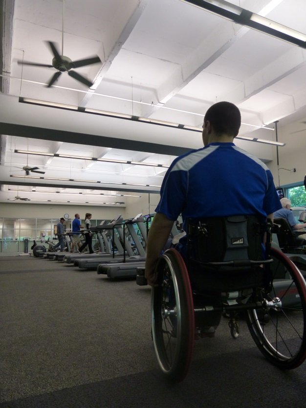 an individual in a wheelchair looks at a row of treadmills in a fitness center
