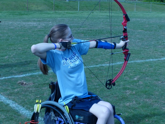 a girl participates in archery, shooting a bow and arrow from a wheelchair