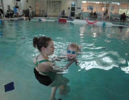 a woman supports a child in front of her body in a pool
