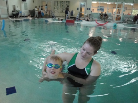 a woman supports a child by holding him at her side as he swims