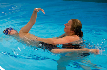 a woman supports a child while he practices a swimming stroke in the pool
