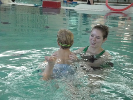 a woman holds a child just under the child's armpits in a pool