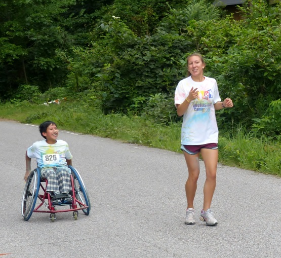 a girl runs alongside a child in a wheelchair