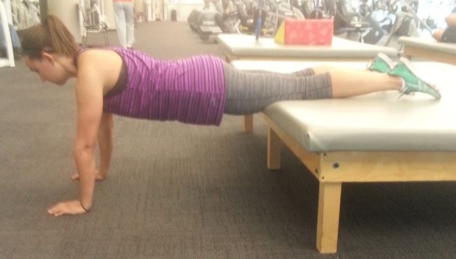 girl does plank with feet elevated on and supported by bench