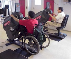 Photo of two SCIFIT machines, one being used by a person in a wheelchair for upper body exercise.