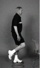 A man is standing next to a chair demonstrating one leg standing on foam