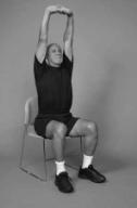 A man is seated on chair demonstrating overhead stretch