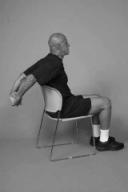 A man is seated on chair demonstrating chest stretch