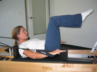 A woman is using the Reformer which uses springs to provide resistance