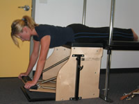 The stability chair exercise is modified by placing the chair at the end of the trapeze table, allowing the legs to be supported