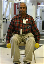 A man is seated demonstrating the start position for a Hammer Bicep Curl with Free Weights exercise