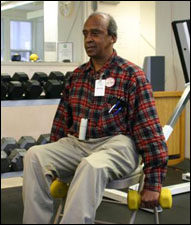 A man is seated demonstrating the start position for a Front Raise with Free Weights - Shoulders exercise.