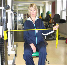 A woman is seated demonstrating an end position for a External Rotation with Thera-Band® exercise