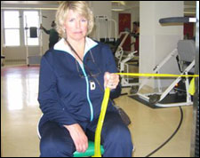 A woman is seated demonstrating a start position for a Internal Rotation with Thera-Band® exercise