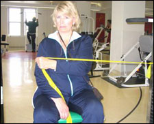 A woman is seated demonstrating an end position for a Internal Rotation with Thera-Band® exercise