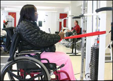 A woman is seated demonstrating a start position for a Reverse Fly with Thera-Band® exercise