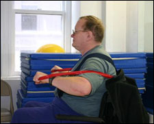 A man is seated demonstrating a start position for a Chest Press with Thera-Band® exercise
