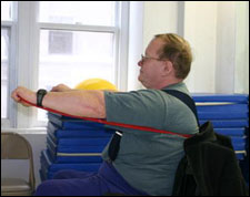 A man is seated demonstrating an end position for a Chest Press with Thera-Band® exercise