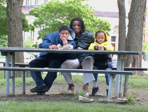A mother sits with her two children a young girl and a middle school aged boy with a developmental disability on a park bench