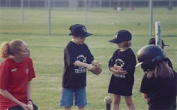 Four small children practice T-ball with a leisure companion watching.