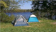 Two tents shown in a grassy area with trees and a lake in the background